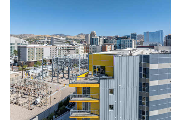 A modern building with a yellow section in the middle is in the foreground of a cityscape. at Paperbox Lofts Apartments, Utah